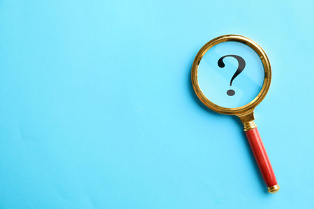 Question mark on light blue background, top view through magnifying glass. Space for text