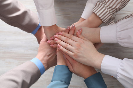 Business concept. Group of people stacking hands at light wooden table, top viewの写真素材