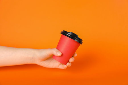 Woman holding paper cup on orange background, closeup. Mockup for design