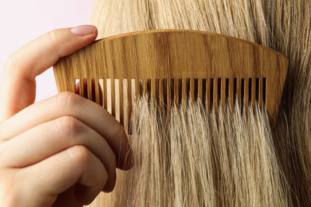 Woman brushing hair with wooden comb on pink background, closeupの写真素材