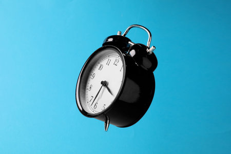 Black alarm clock in air on light blue background