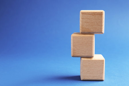 Stack of wooden cubes on blue background, closeup. Space for text