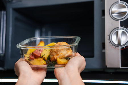Woman putting container with lunch into microwave indoors, closeupの写真素材