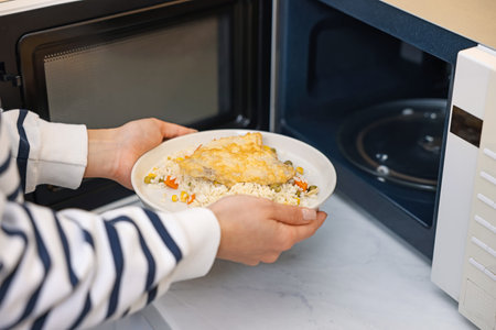 Woman putting plate with lunch into microwave indoors, closeupの写真素材
