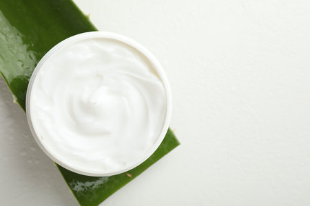 Moisturizing cream with extract of aloe vera and cut leaf on white background, top view. Space for textの写真素材