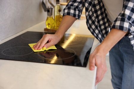 Man cleaning electric stove with rag in kitchen, closeupの写真素材
