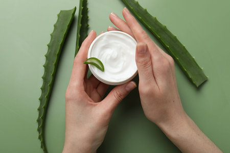 Woman with moisturizing cream and aloe vera leaves on green background, top viewの写真素材