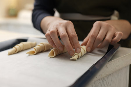 Woman putting raw croissants onto baking sheet at wooden table indoors, closeupの写真素材