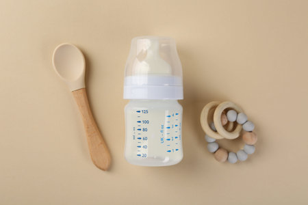 Feeding bottle with milk, spoon and teether on beige background, flat layの写真素材