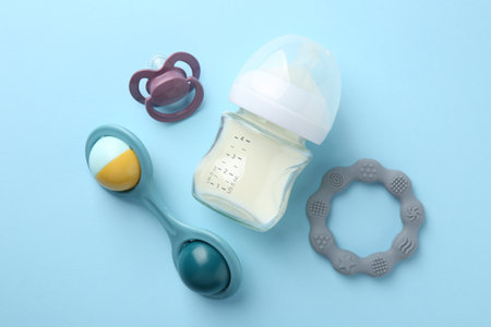 Feeding bottle with milk, baby rattle, teether and pacifier on light blue background, flat layの写真素材