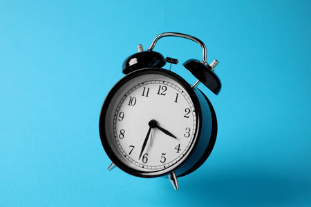Black alarm clock in air on light blue backgroundの写真素材