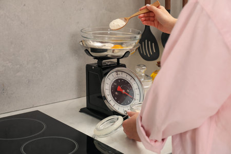 Woman adding flour into bowl on mechanical kitchen scale at white marble countertop indoors, closeupの写真素材