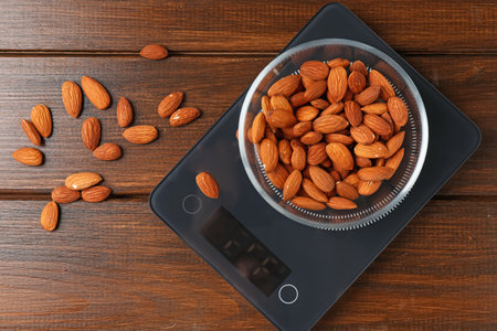 Electronic kitchen scale with bowl of almond nuts on wooden table, flat layの写真素材