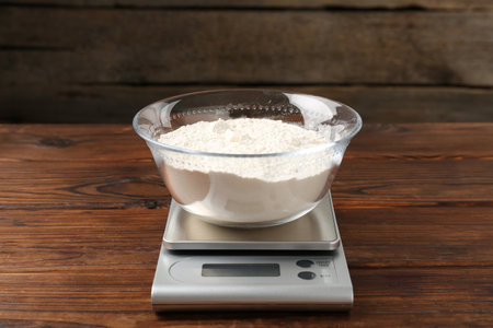 Electronic kitchen scale with bowl of flour on wooden table, closeupの写真素材