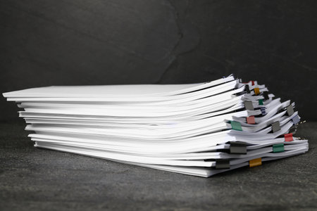 Colorful binder clips with sheets of paper on dark textured table, closeupの写真素材