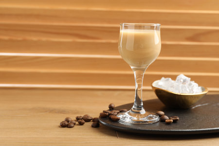 Coffee cream liqueur in glass, ice and beans on wooden table, space for text