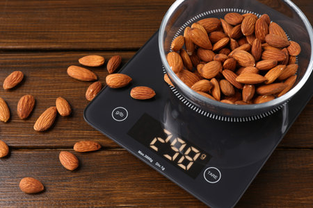 Electronic kitchen scale with bowl of almond nuts on wooden table, closeupの写真素材