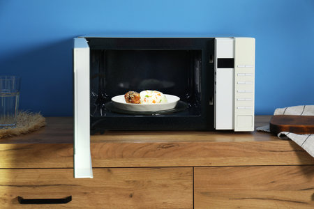 Open microwave oven with cooked rice and chicken on wooden cabinet indoorsの写真素材