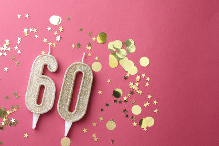 60th birthday. Number shaped candles and confetti on pink background, flat lay. Space for textの写真素材