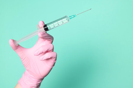 Doctor holding syringe with medication on turquoise background, closeup. Space for textの写真素材