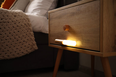 Glowing modern LED lamp on wooden bedside table indoors, closeupの写真素材