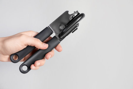 Woman holding can opener against light background, closeup. Space for textの写真素材