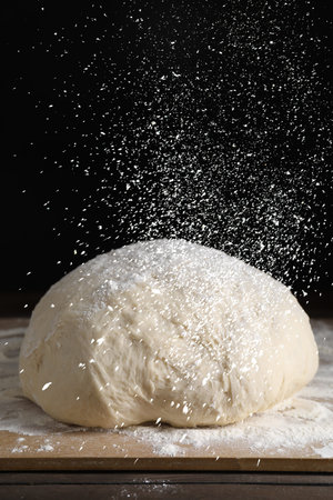 Sprinkling flour over dough on table, closeup