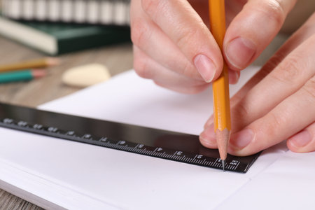 Woman drawing sketch with ruler and pencil on notebook at table, closeup