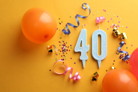40th birthday. Number shaped candles and party decor on orange background, flat lay
