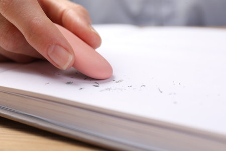 Woman rubbing eraser against paper at wooden table, closeup