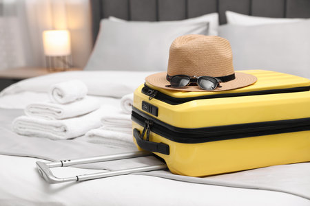 Suitcase with hat and sunglasses on bed in hotel roomの写真素材