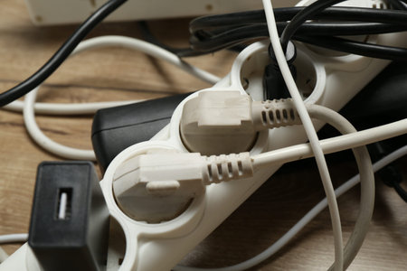 Extension power boards overloaded with plugs on wooden floor, closeup