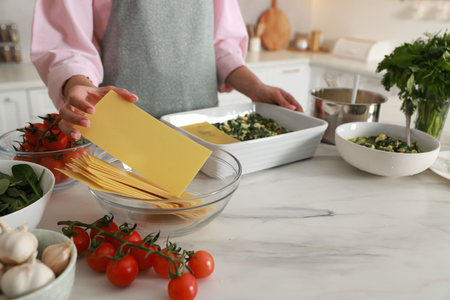Woman making spinach lasagna at marble table indoors, closeupの写真素材