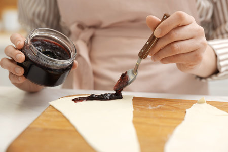 Woman spreading jam onto fresh dough at white table, closeup. Making croissantsの写真素材