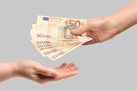 Hand giving banknotes to another hand on grey background, closeupの写真素材