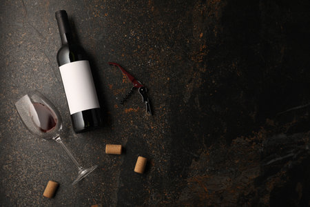 Bottles of wine, glass, corks and corkscrew on dark table, flat lay. Space for textの写真素材