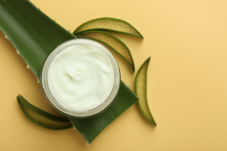 Moisturizing cream with extract of aloe vera in jar and cut leaves on yellow background, flat lay. Space for textの写真素材