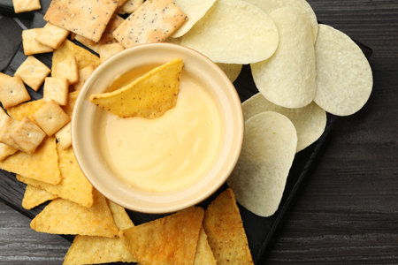 Tasty cheese dipping sauce in bowl and different snacks on dark wooden table, top viewの写真素材