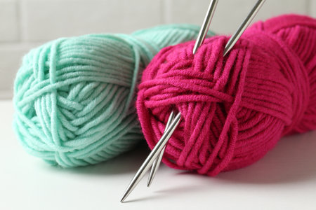 Skeins of colorful yarn and knitting needles on white table, closeupの写真素材