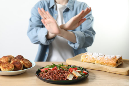 Woman refusing to eat products at wooden table near white brick wall, selective focus. Food allergy conceptの写真素材