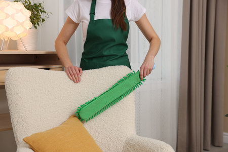 Janitor cleaning armchair with duster at home, closeup