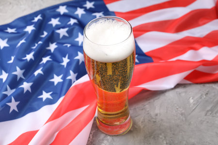 Glass of beer and American flag on grey tableの写真素材