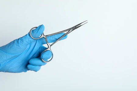 Doctor with surgical forceps on white background, closeup. Space for text