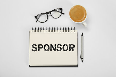 Word Sponsor in notebook, pen, coffee and eyeglasses on white table, top viewの写真素材