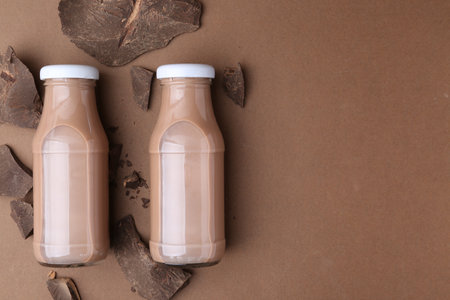 Tasty chocolate milk in glass bottles and pieces of chocolate on brown background, flat lay. Space for textの写真素材