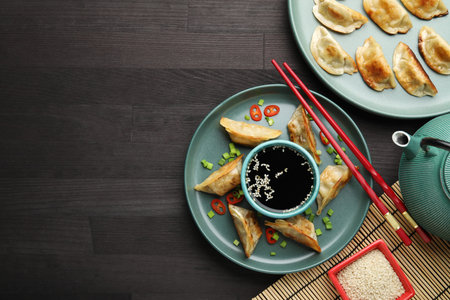 Delicious fried gyoza dumplings with green onions and chili peppers served on wooden table, flat...