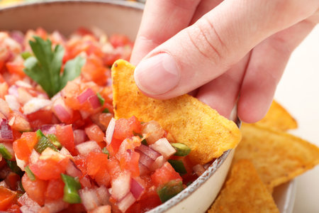 Woman dipping nacho chip into delicious salsa sauce at table, closeupの写真素材