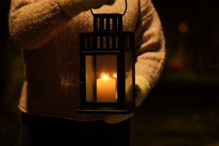 Woman holding Christmas lantern with burning candle in darkness, closeupの写真素材