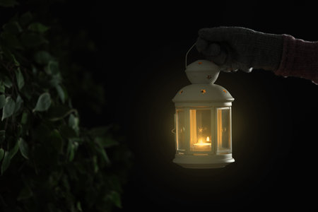 Woman holding Christmas lantern with burning candle on dark background, closeupの写真素材