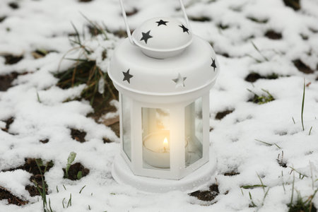 Christmas lantern with burning candle in snowy parkの写真素材